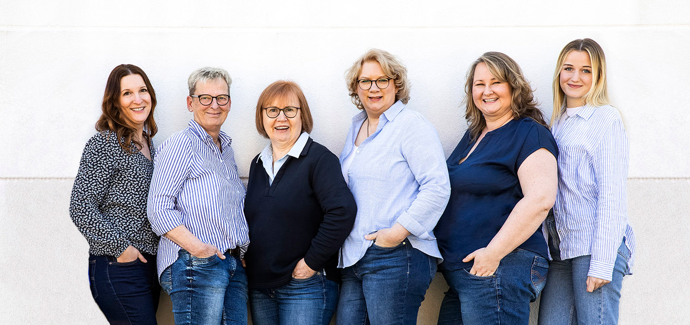 das ganze Team, 7 weibliche Personen stehen zusammen vor einer weißen Wand